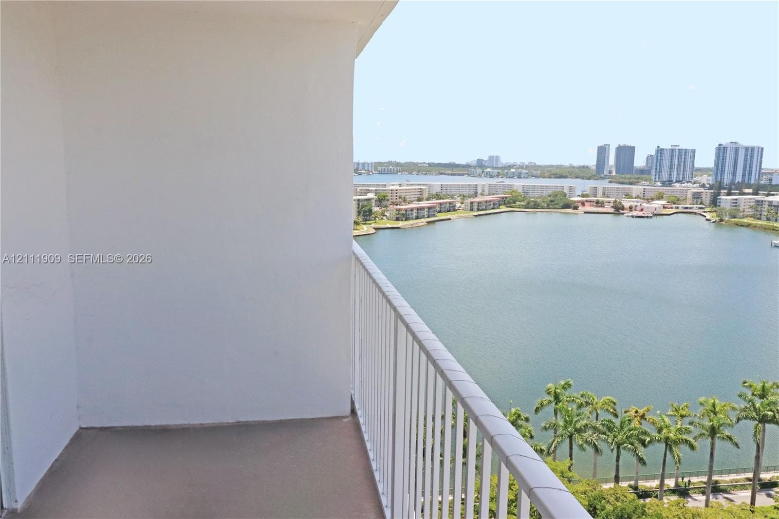 Covered balcony featuring concrete flooring and a vertical bar metal railing, overlooking an expansive lake and urban skyline