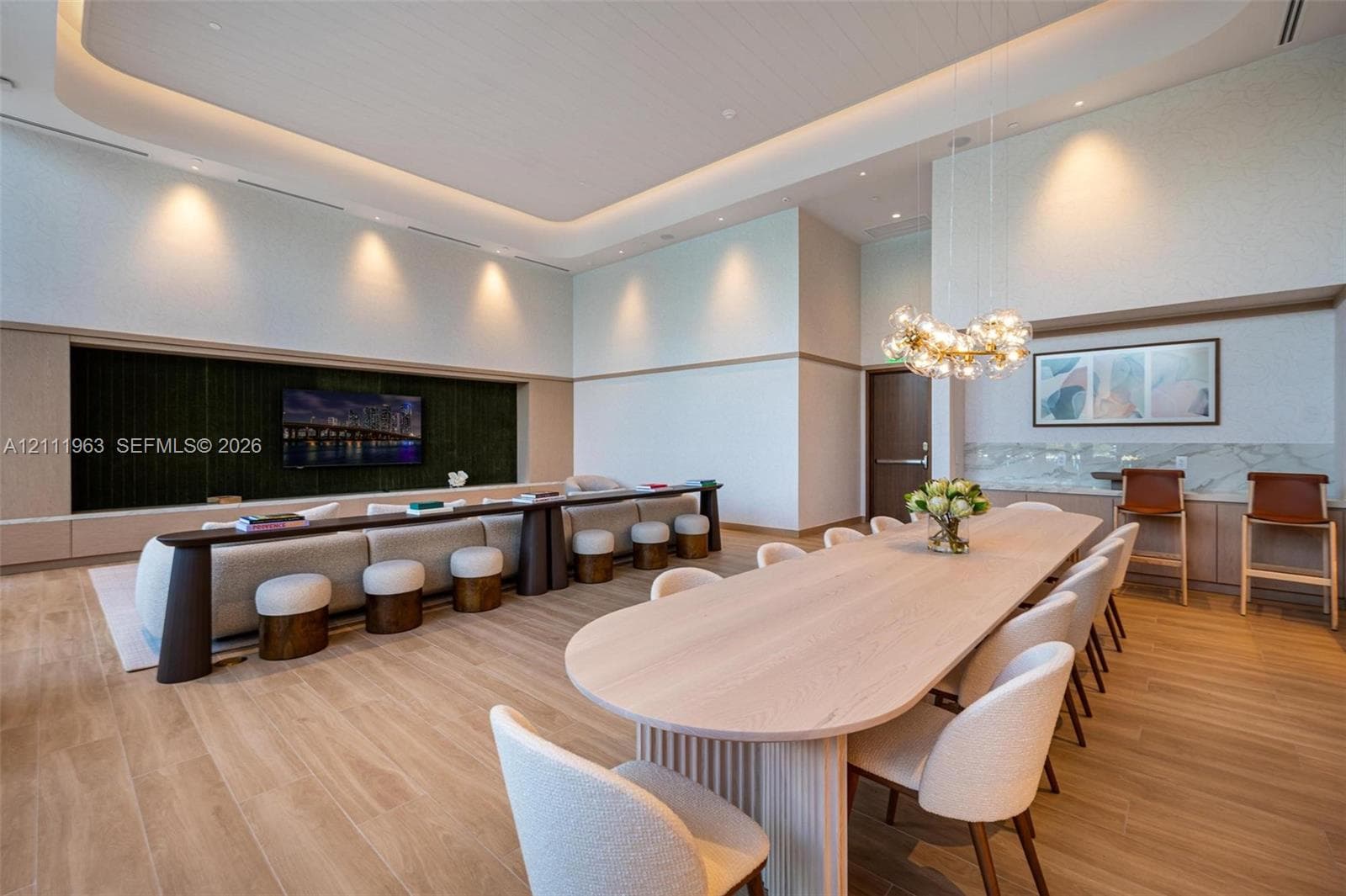 High-ceiling living area featuring recessed cove lighting, wood-finish flooring, custom built-in cabinetry with integrated media wall, and a multi-globe pendant light fixture