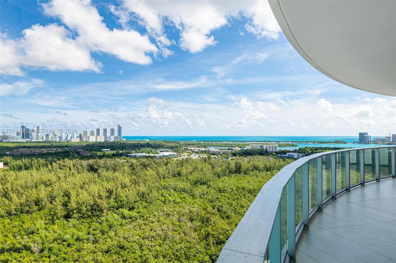 Curved balcony featuring large-format tile flooring and frameless glass railings, overlooking an expansive landscape and coastal horizon