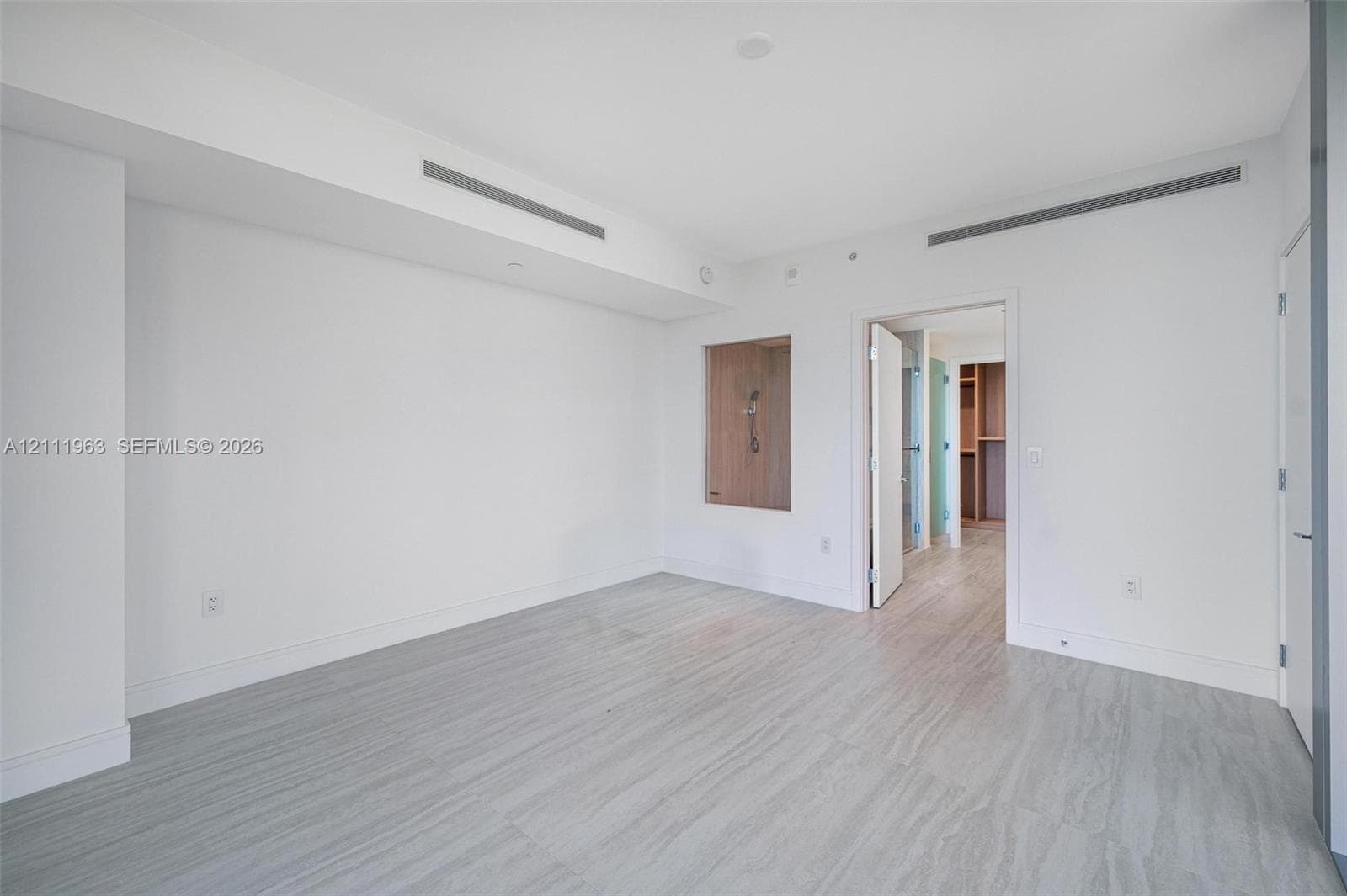 Neutral interior space featuring recessed linear ceiling diffusers, light-toned wood-finish flooring, a built-in recessed wall niche, and minimalist solid-core doors