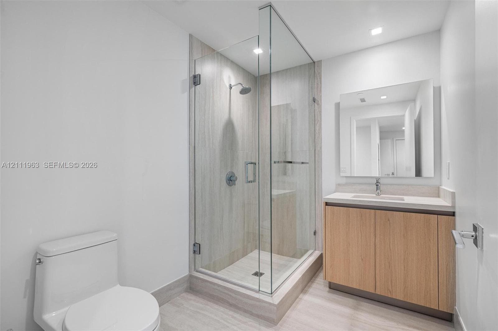 Bathroom featuring a glass-enclosed shower with floor-to-ceiling tile surround, floating wood-finish vanity with a rectangular sink, quartz countertop, and a frameless wall-mounted mirror
