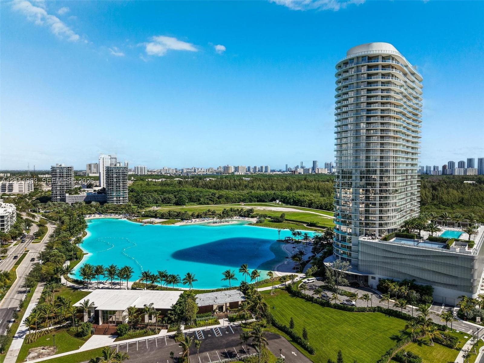 High-rise residential tower featuring wrap-around balconies, an expansive turquoise lagoon, palm-lined shorelines, and manicured green spaces
