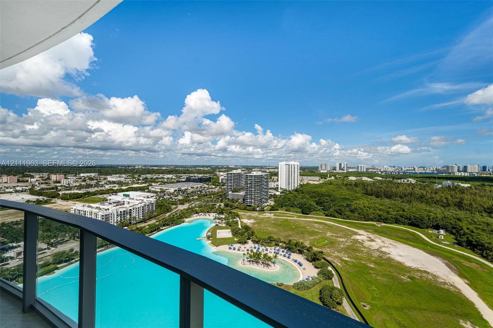 Elevated balcony featuring glass railings and panoramic landscape scenery including a man-made lagoon and coastal horizon