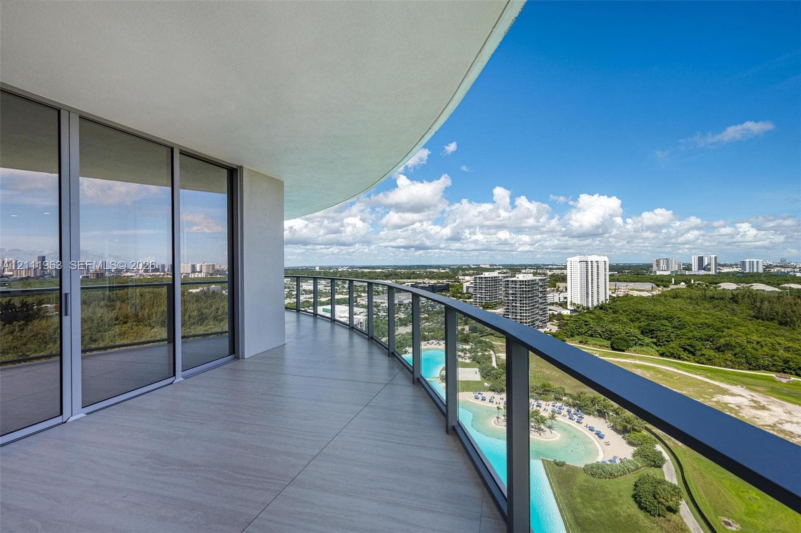 Curved balcony featuring large-format tile flooring, a glass-panel railing, and full-height floor-to-ceiling sliding glass doors