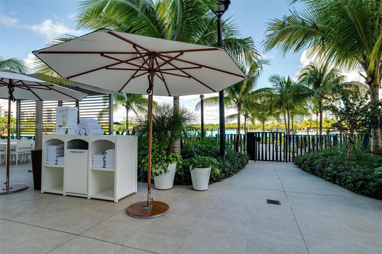Outdoor terrace featuring large-format stone tile flooring, perimeter landscaping with mature palms, and a built-in white service station