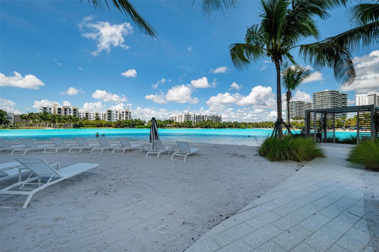 Sandy shoreline with turquoise water, palm trees, and a paved walkway