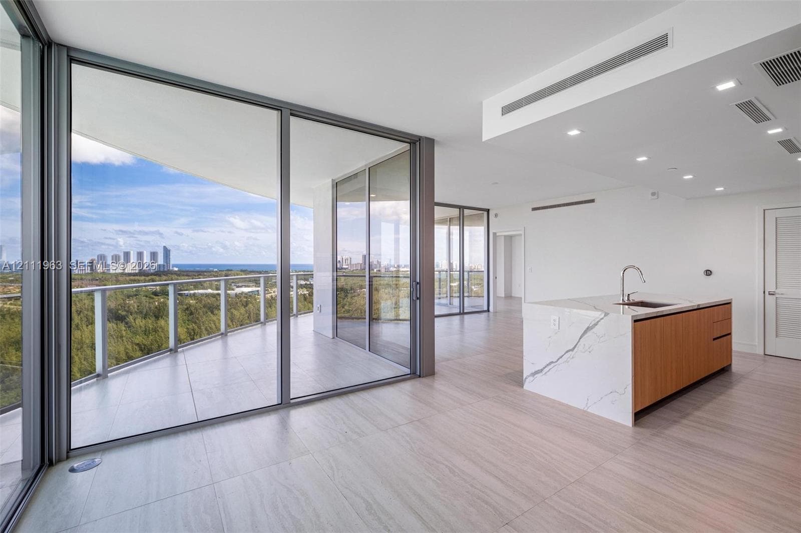 Floor-to-ceiling glass walls, expansive wraparound terrace with metal railings, kitchen island featuring waterfall-edge stone countertop, wood-finish cabinetry, and large-format tile flooring