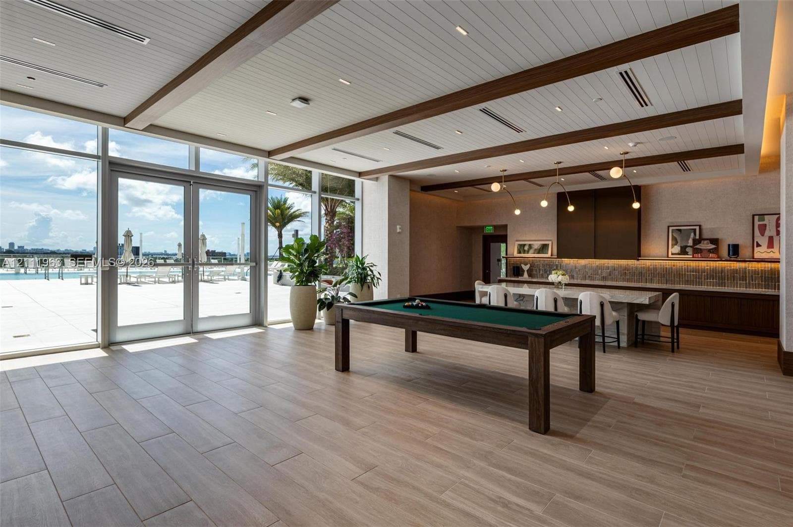 Floor-to-ceiling glass panel doors, wood-finish plank flooring, ceiling with exposed decorative beams, integrated recessed lighting, and built-in bar cabinetry with stone-surface counters