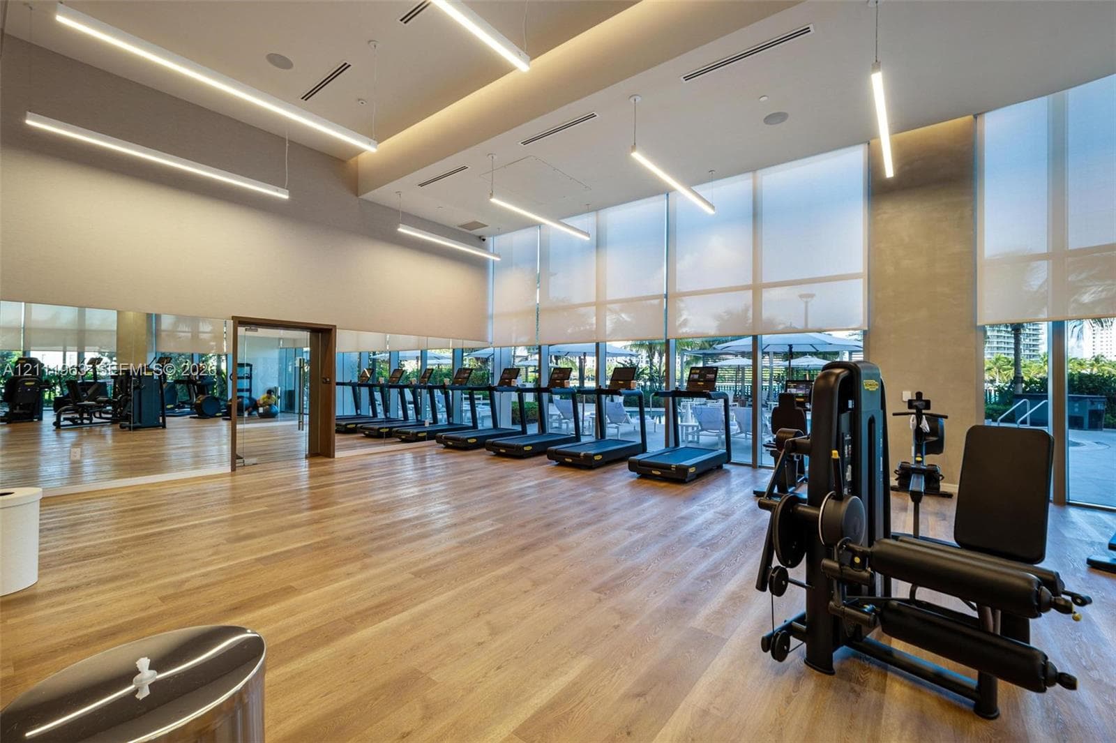 Fitness center featuring wood-finish flooring, floor-to-ceiling windows with roller shades, linear pendant lighting, and wall-to-wall mirrors