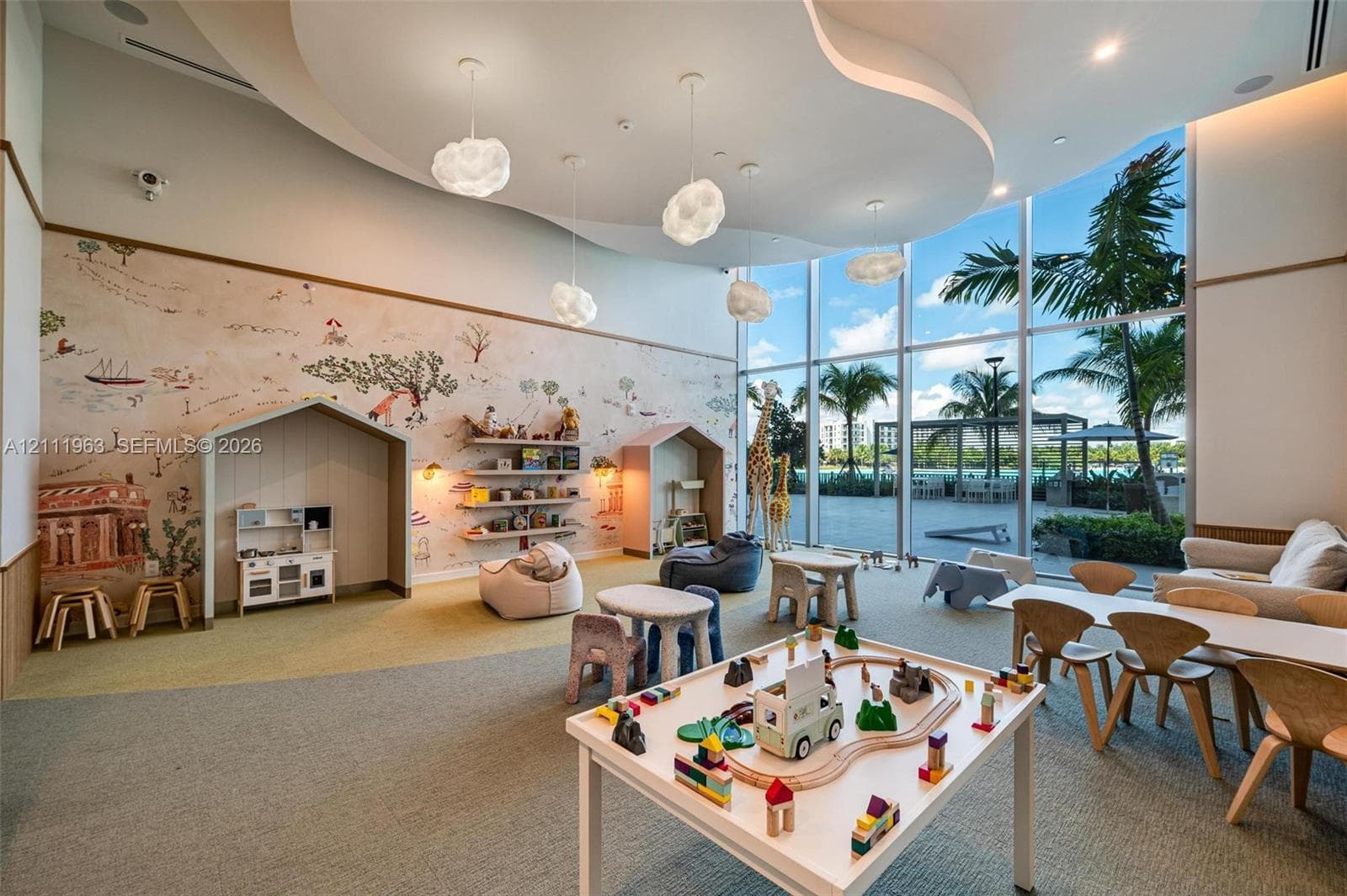 Expansive room featuring floor-to-ceiling glass windows, recessed ceiling architecture with cloud-shaped pendant lighting, and custom wall-mounted shelving with built-in reading nooks