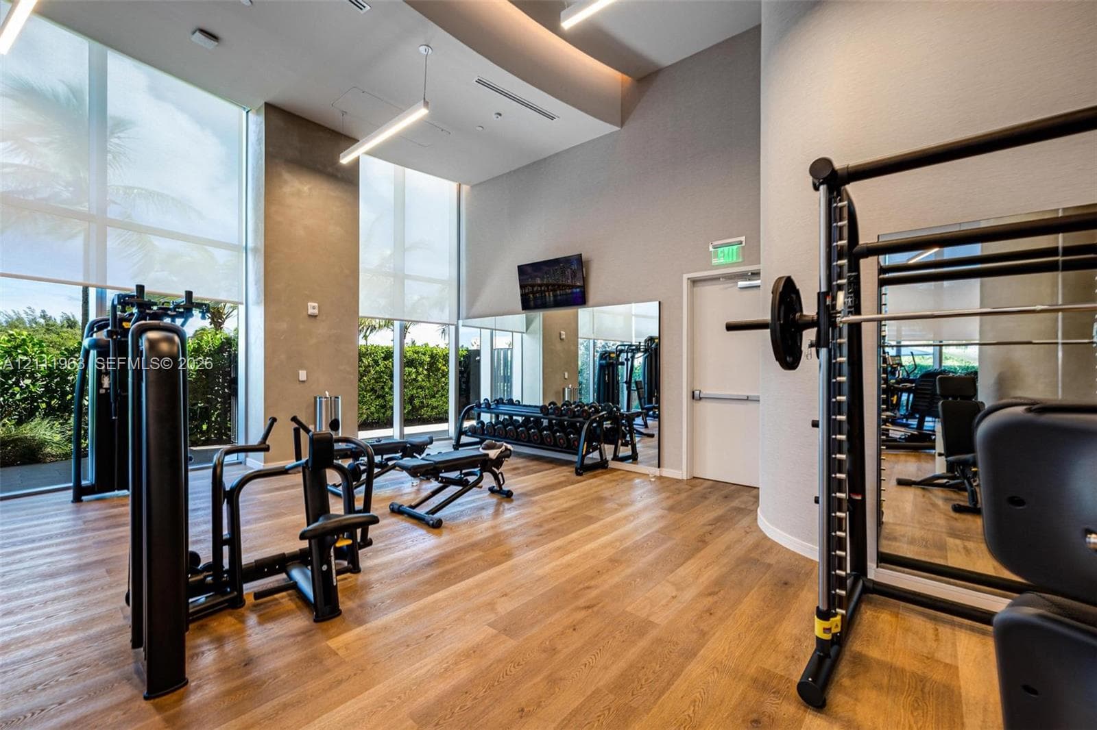 Fitness facility featuring floor-to-ceiling windows, wood-finish flooring, recessed tray ceiling lighting, and large wall-mounted mirrors
