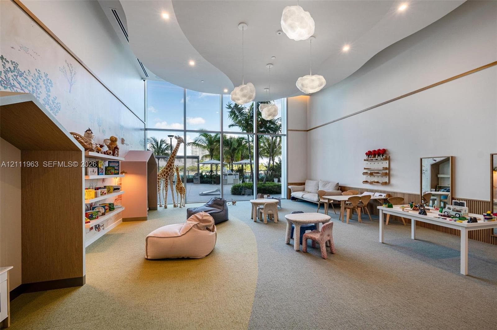 Expansive room featuring floor-to-ceiling windows, custom built-in wood shelving, intricate tray ceiling detail, recessed lighting, and sculptural pendant fixtures