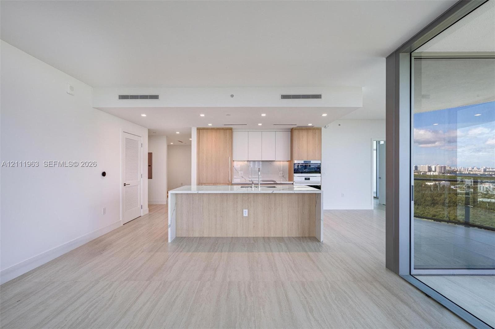 Kitchen featuring wood-finish cabinetry, stone-surface center island with integrated sink, built-in wall oven, recessed lighting, and expansive floor-to-ceiling glass sliding doors