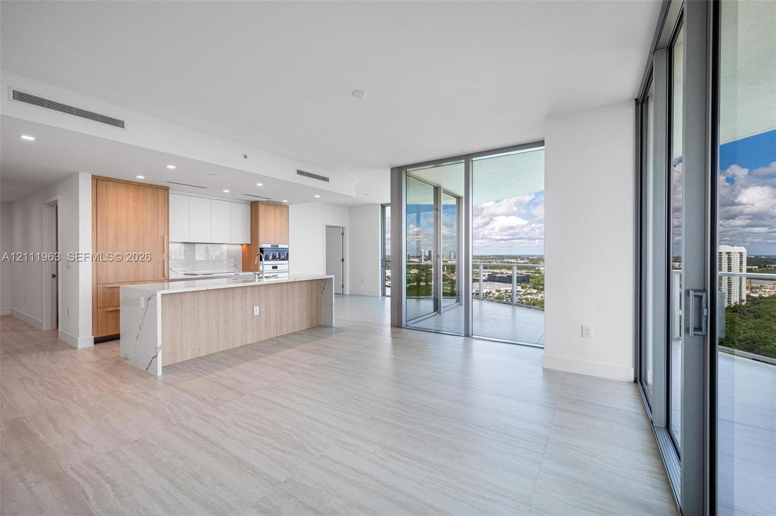 Open-concept kitchen featuring wood-finish cabinetry, white slab cabinetry, stone-surface countertops, recessed lighting, and floor-to-ceiling glass sliding doors