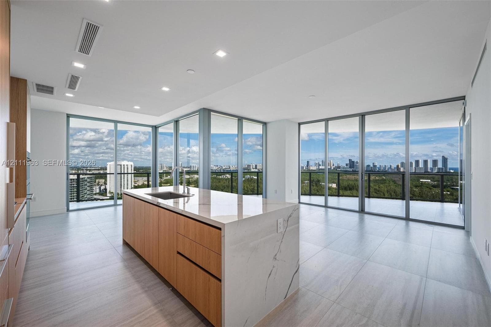 Kitchen island featuring stone-finish waterfall countertops and wood-finish cabinetry, floor-to-ceiling glass panel walls, and large-format tile flooring