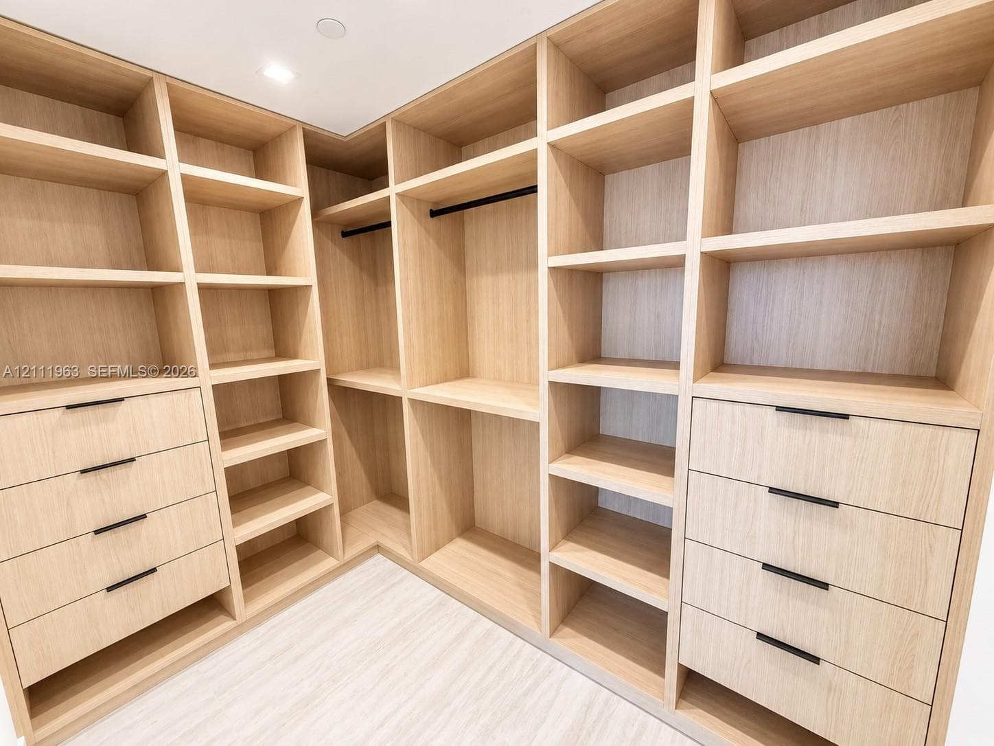 Custom floor-to-ceiling built-in cabinetry featuring light wood-finish shelving, multiple integrated hanging rods, and drawers with matte black pulls