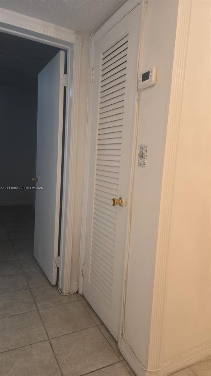 White louvered closet door featuring a brass-finished knob and digital thermostat