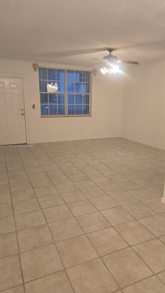 Interior space featuring large-format neutral tile flooring, a multi-pane window with a grid pattern, and a ceiling fan with integrated multi-bulb light fixture
