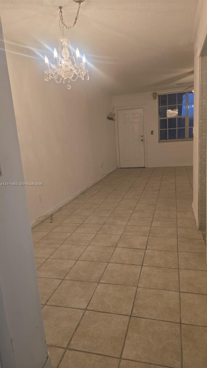 Interior area featuring neutral square tile flooring, a multi-arm chandelier with crystal accents, and a grid-pane window