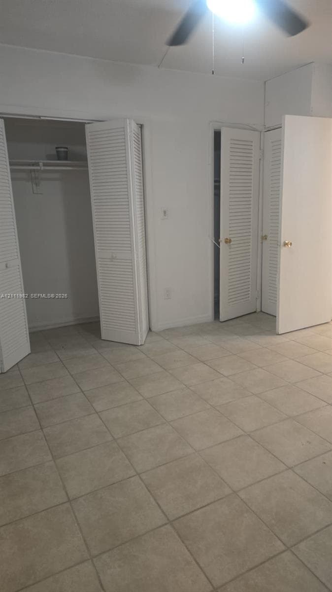 Interior space featuring neutral floor tiling, louvered closet doors, and a ceiling-mounted light fixture with a fan