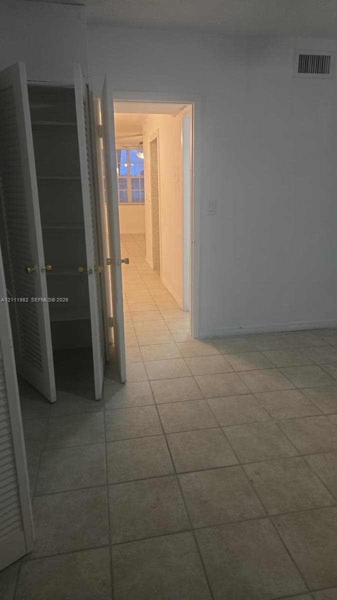 Neutral-toned tile flooring, built-in storage closet with louvered doors, and light-colored interior walls