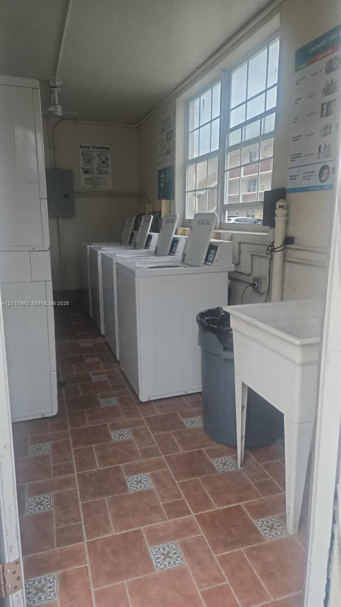 Dedicated laundry room featuring multi-unit washing machines, a utility sink, large-pane grid windows, and decorative ceramic tile flooring