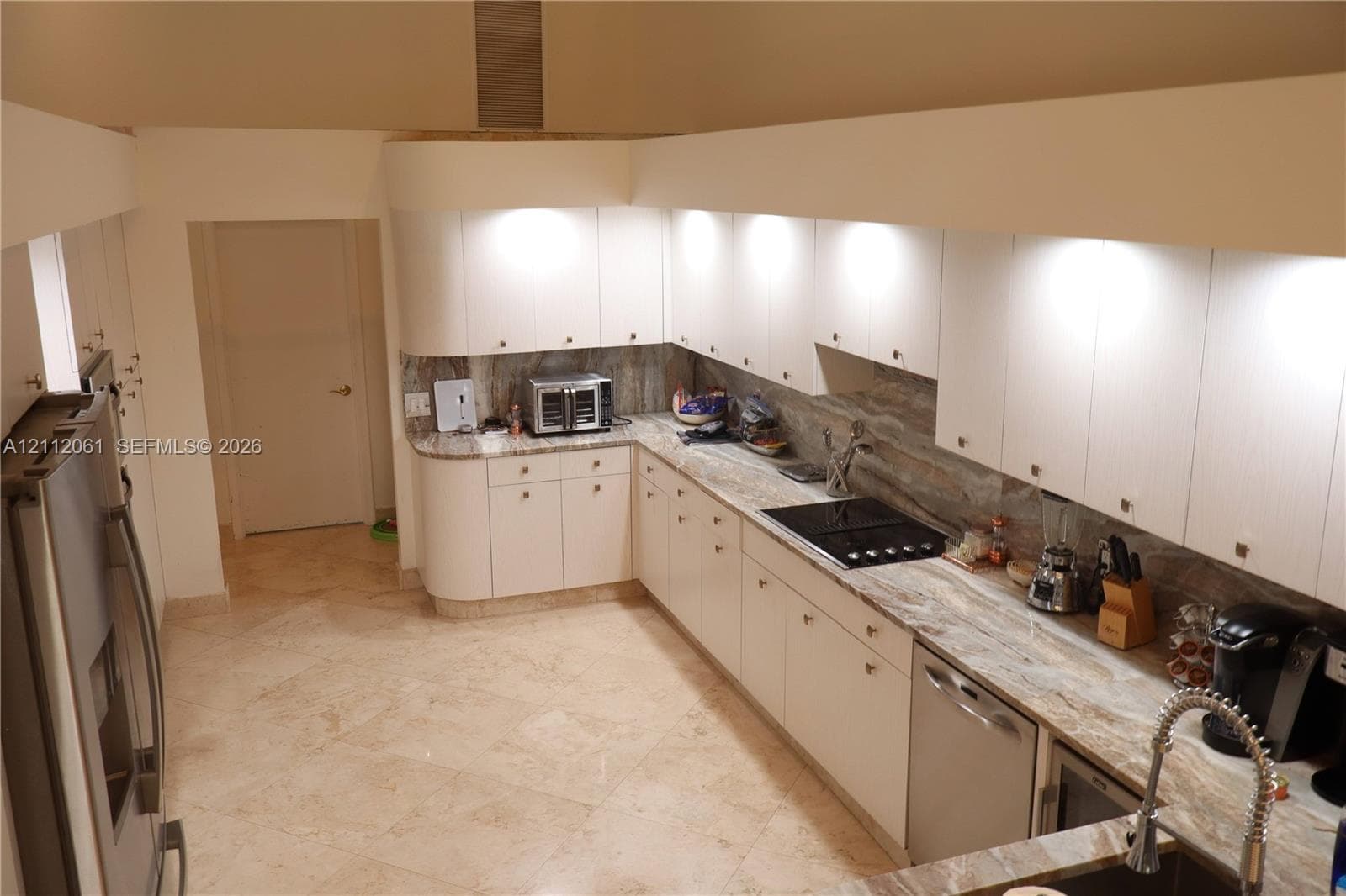 Kitchen featuring light wood laminate cabinetry, pull out pantry ,solid marble countertops, matching marble backsplash, stainless steel appliances, wine fridge,and 24" marble flooring, dramatic high ceilings