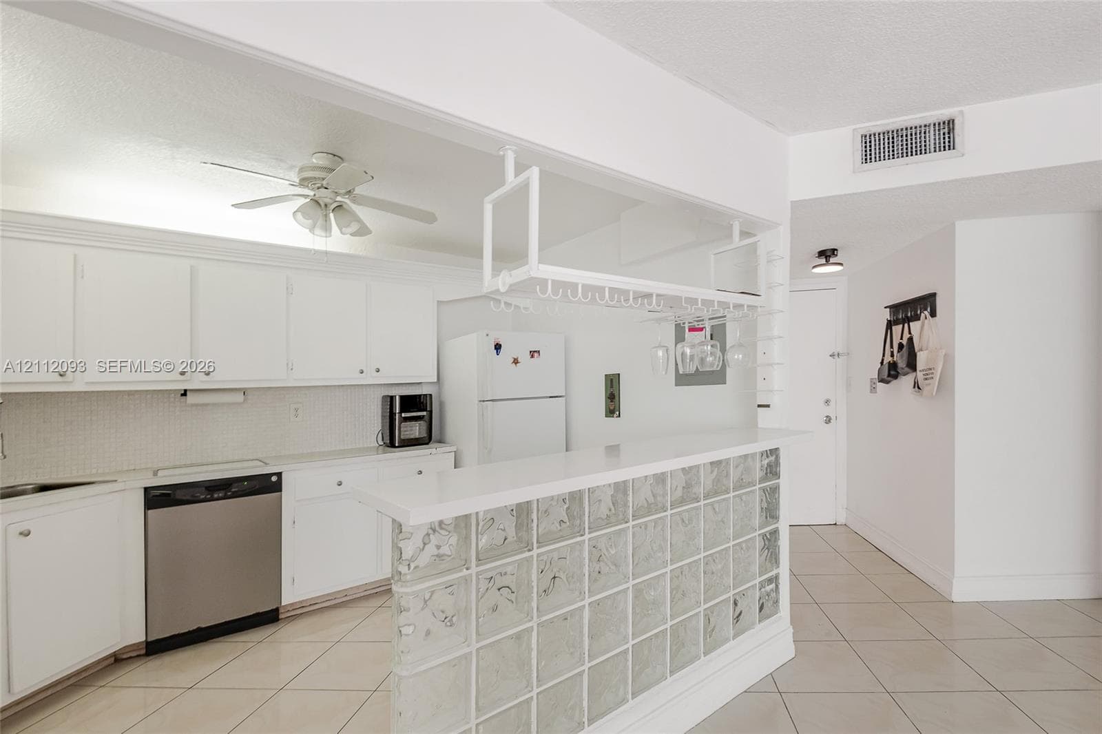 Kitchen featuring white cabinetry, solid-surface breakfast bar with a glass block base, overhead stemware rack, and tile flooring