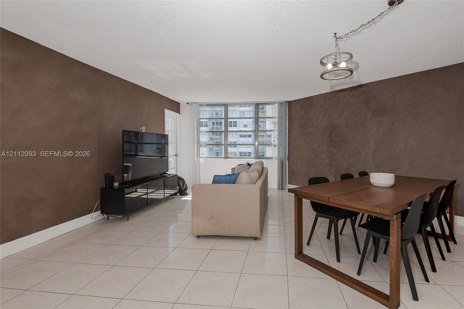 Open-concept interior featuring light-toned tile flooring, textured brown accent walls, and oversized windows with a metallic frame