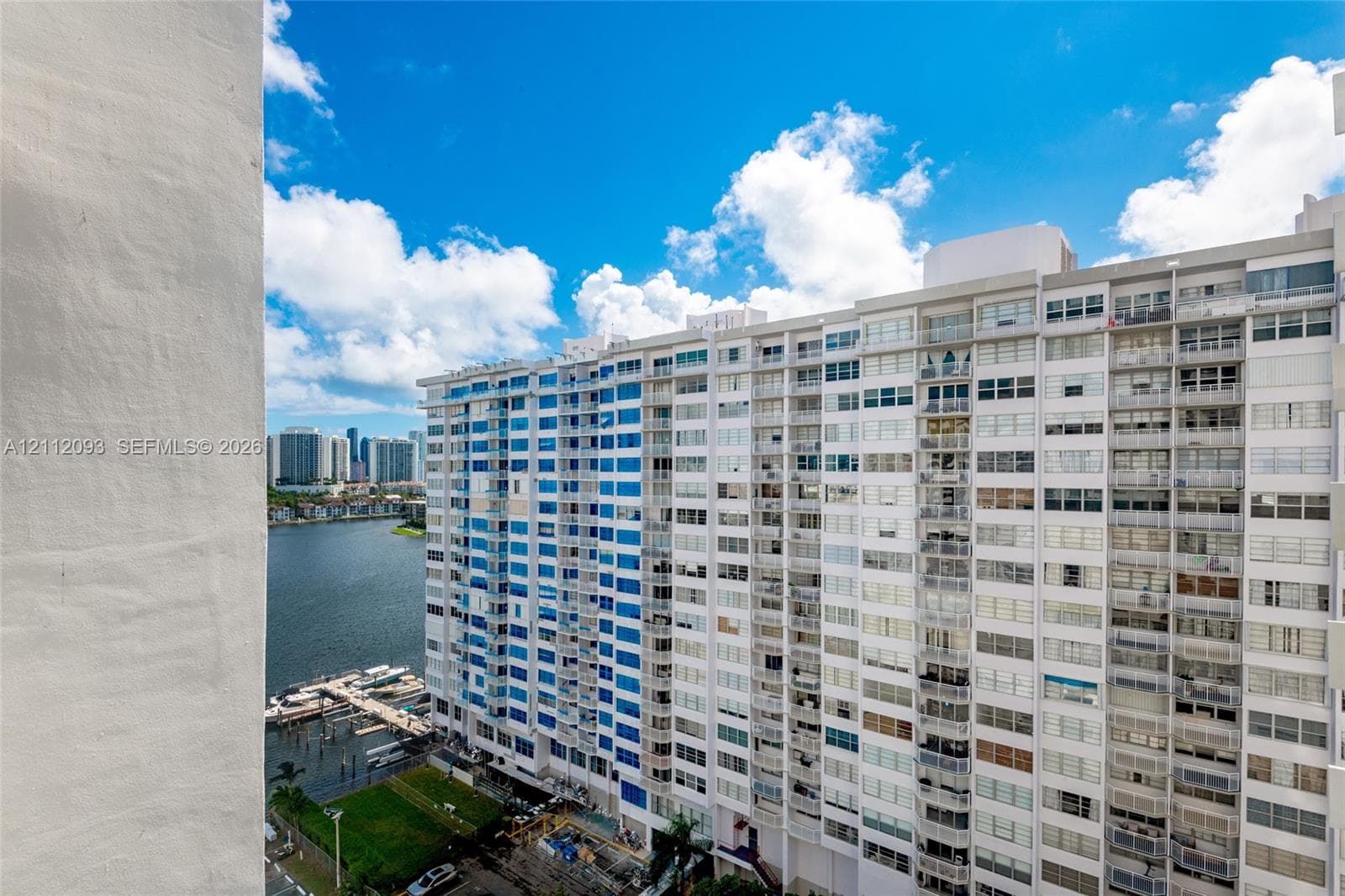 High-rise exterior featuring integrated balconies, floor-to-ceiling windows, and white masonry cladding, overlooking a coastal waterway and dock area