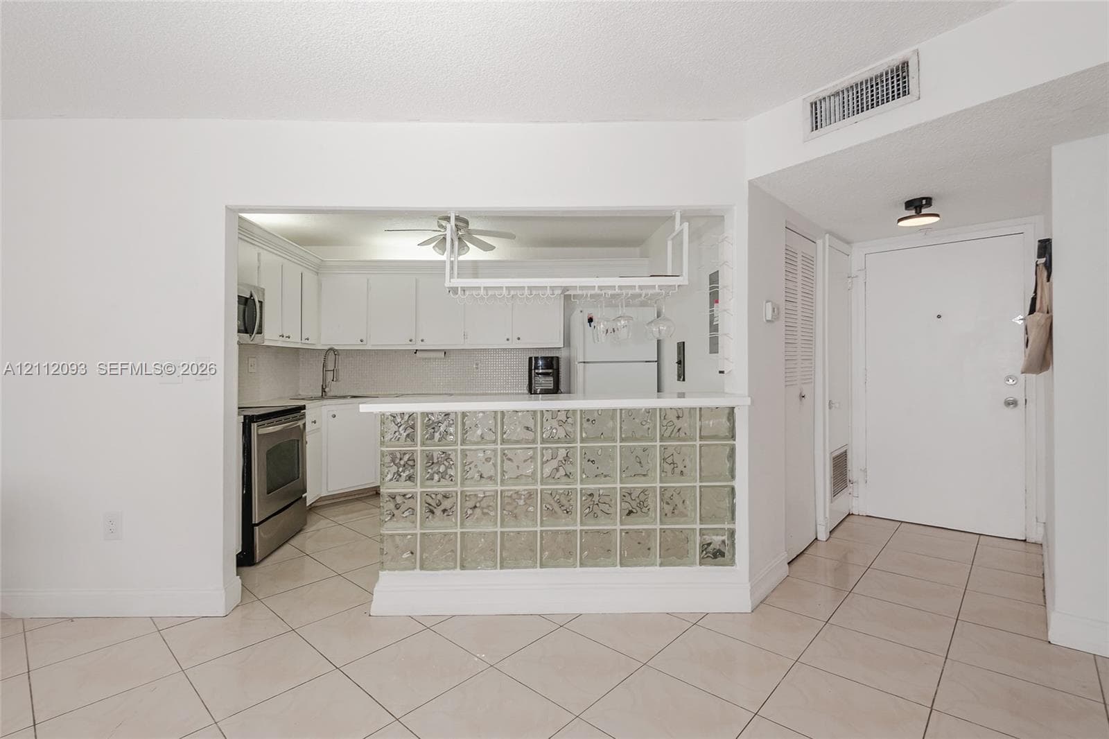 Kitchen featuring white cabinetry, stainless steel appliances, a glass-block breakfast bar, and a hanging stemware rack over ceramic tile flooring