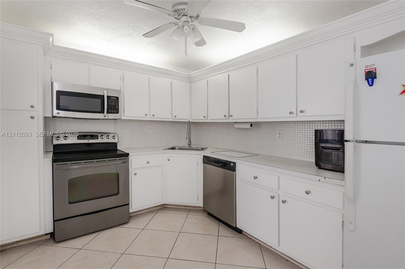Kitchen featuring white cabinetry with crown molding, stainless steel appliances, tiled backsplash, and ceramic tile flooring