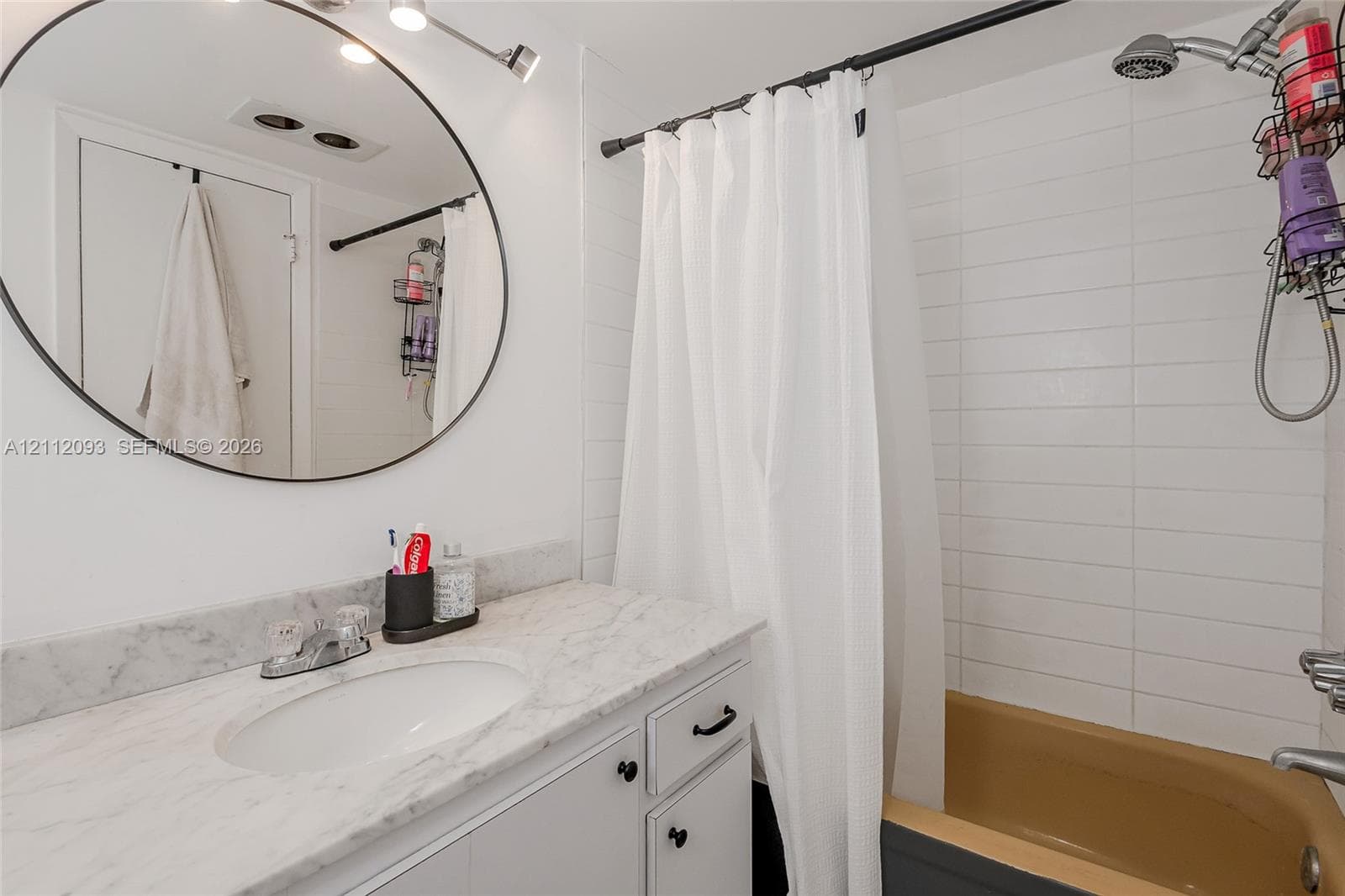Stone-topped vanity with an integrated oval sink, circular wall-mounted mirror, and white horizontal tile wall surround in the shower area