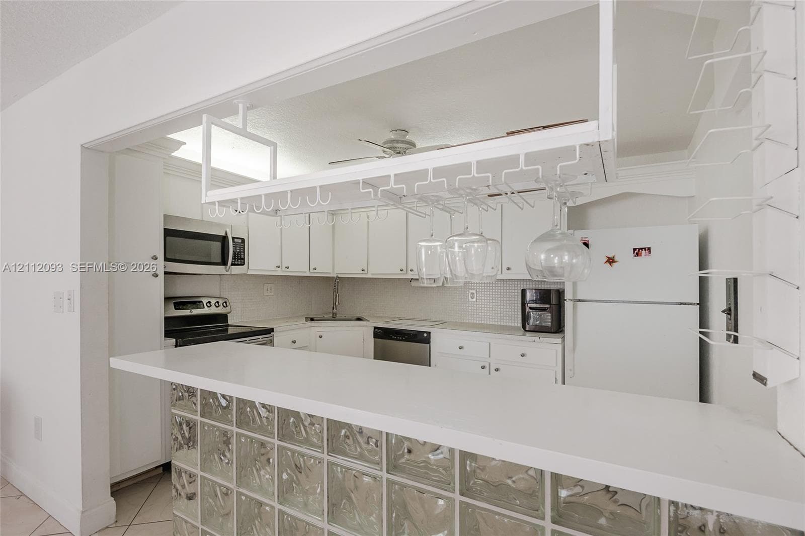 Kitchen featuring white cabinetry, solid-surface breakfast bar, glass block base, and built-in overhead stemware rack