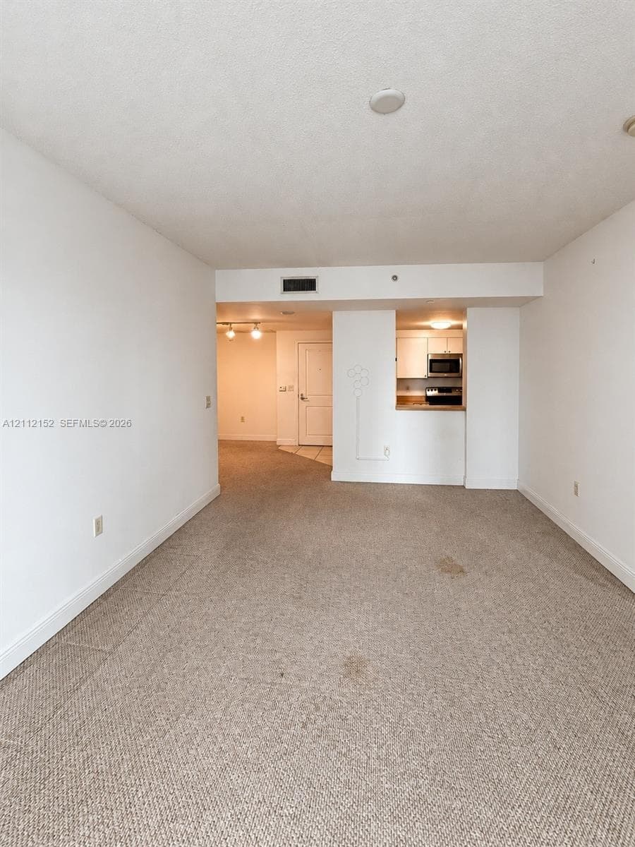 Open interior area featuring wall-to-wall carpeting and a kitchen with built-in cabinetry and integrated appliances