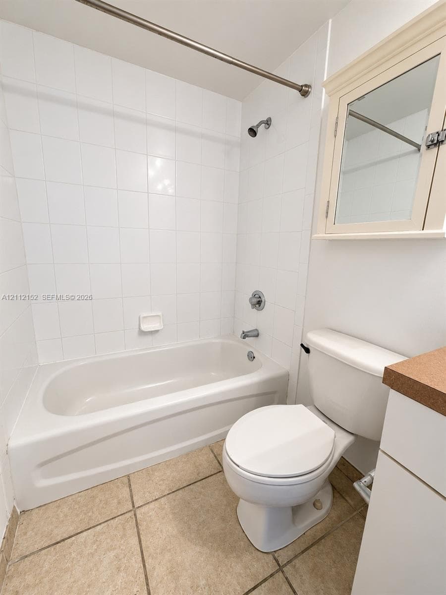 Bathroom featuring tile flooring, a tub-shower combination with full-height wall tiling, built-in medicine cabinet, and a solid-surface vanity countertop