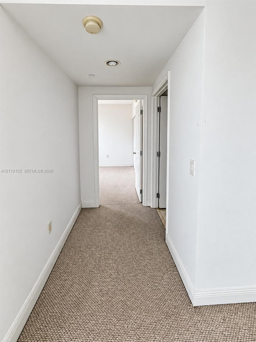 Hallway featuring neutral wall-to-wall carpeting, crisp white interior doors, and recessed ceiling lighting