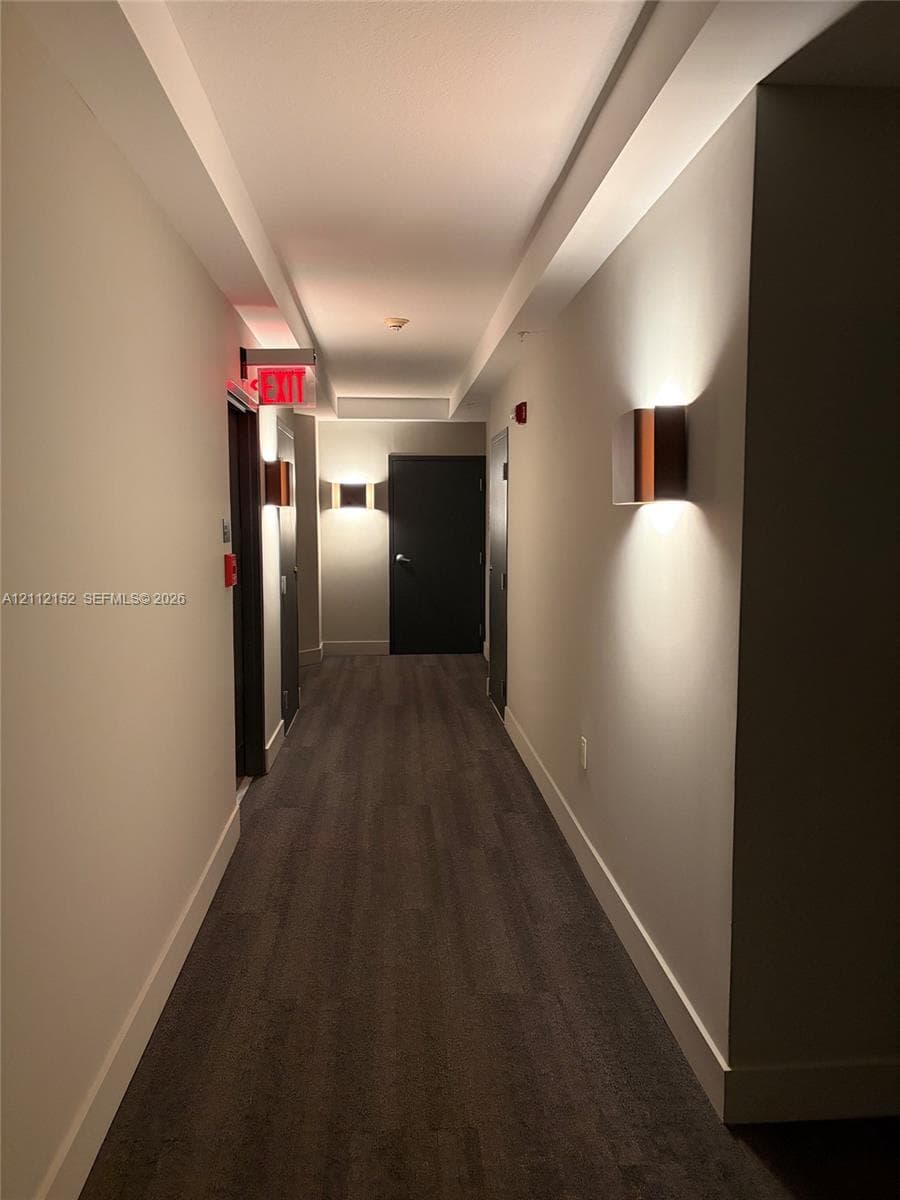Hallway featuring wood-finish flooring, recessed ceiling lighting, and wall-mounted sconces