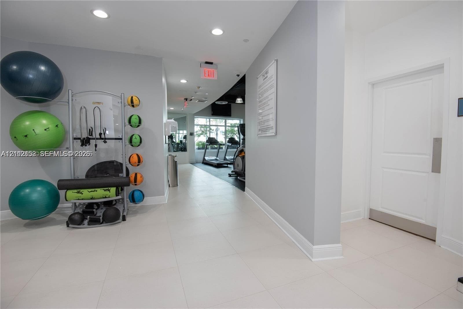 Fitness area featuring large-format tile flooring, recessed lighting, and a multi-panel door with metal kick plate