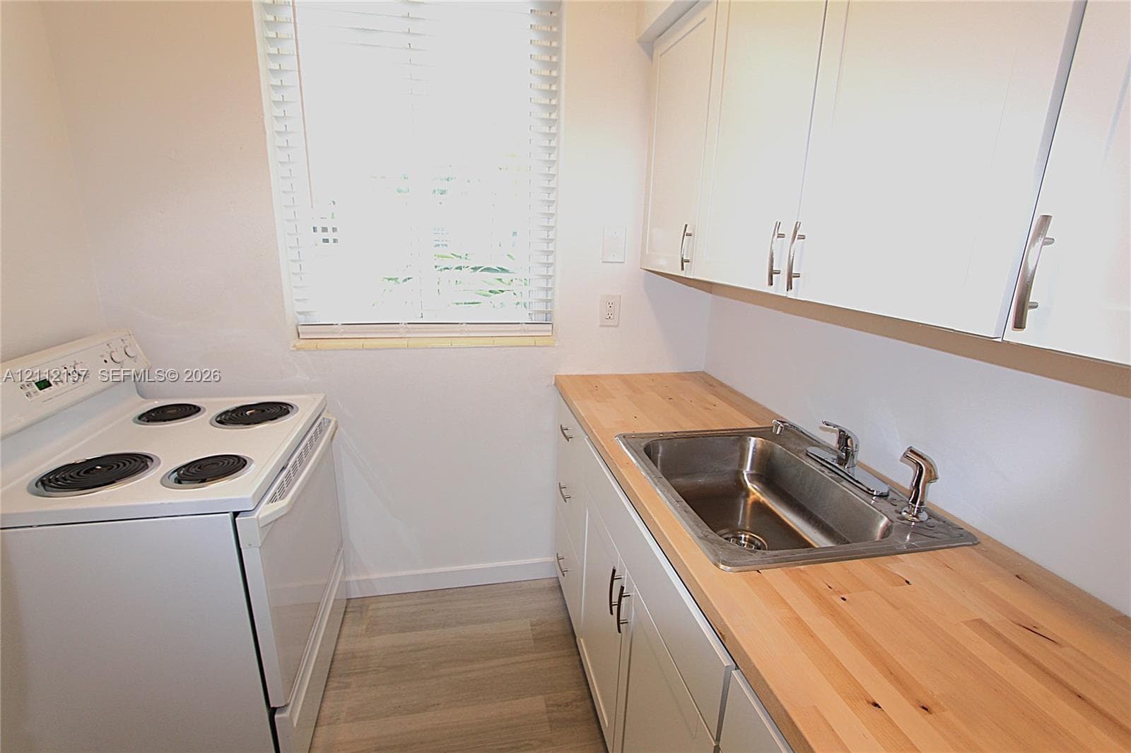 Kitchen featuring white cabinetry, wood-finish countertops, stainless steel sink with a side sprayer, white electric range, and wood-finish flooring