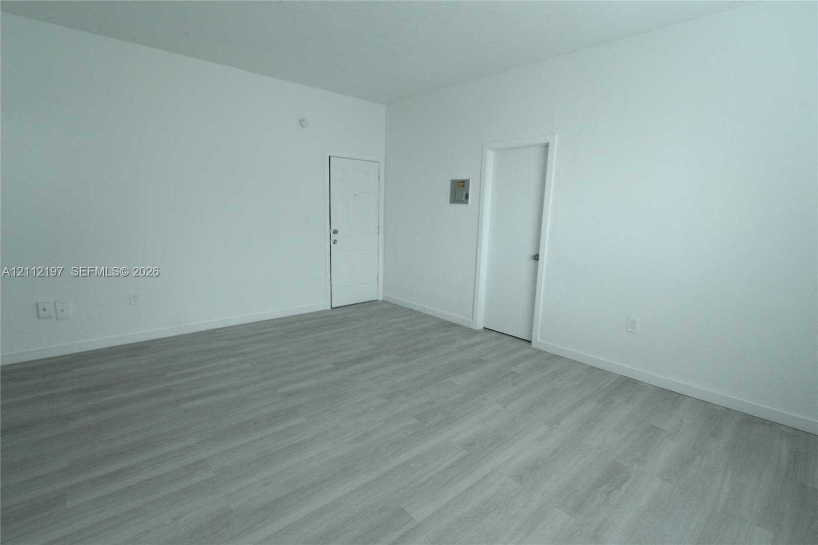Neutral interior room featuring wood-finish flooring, smooth white wall finishes, and two solid-core doors