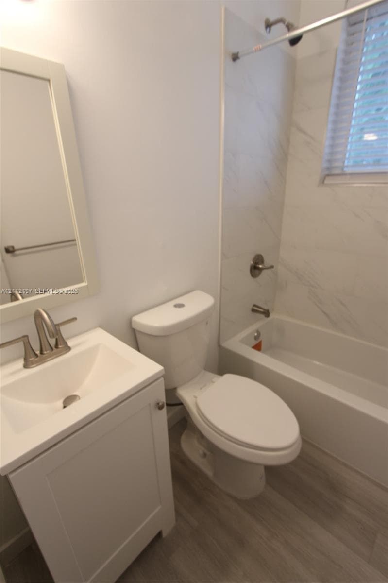 Bathroom featuring a single-sink vanity with a rectangular basin, wood-finish flooring, and a tub-shower combination with light-toned wall tile