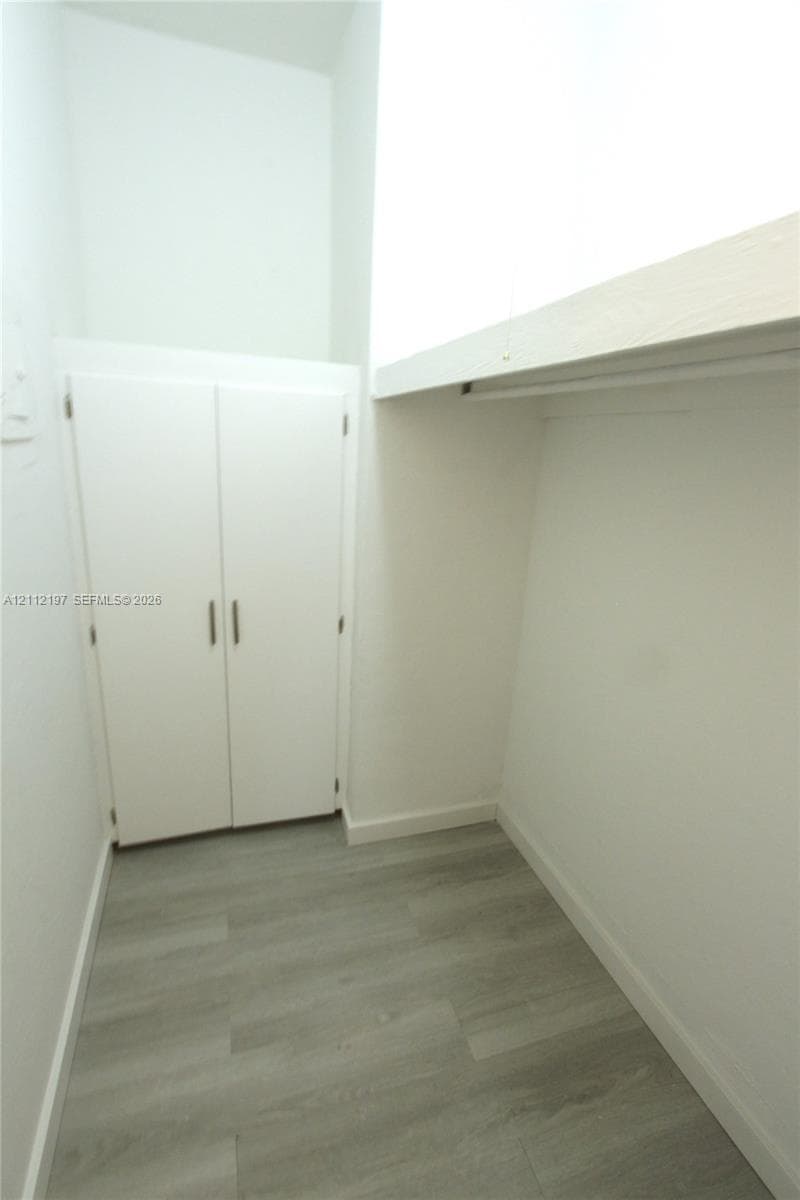Storage area featuring wood-finish flooring, a double-door closet, and an overhead built-in shelf