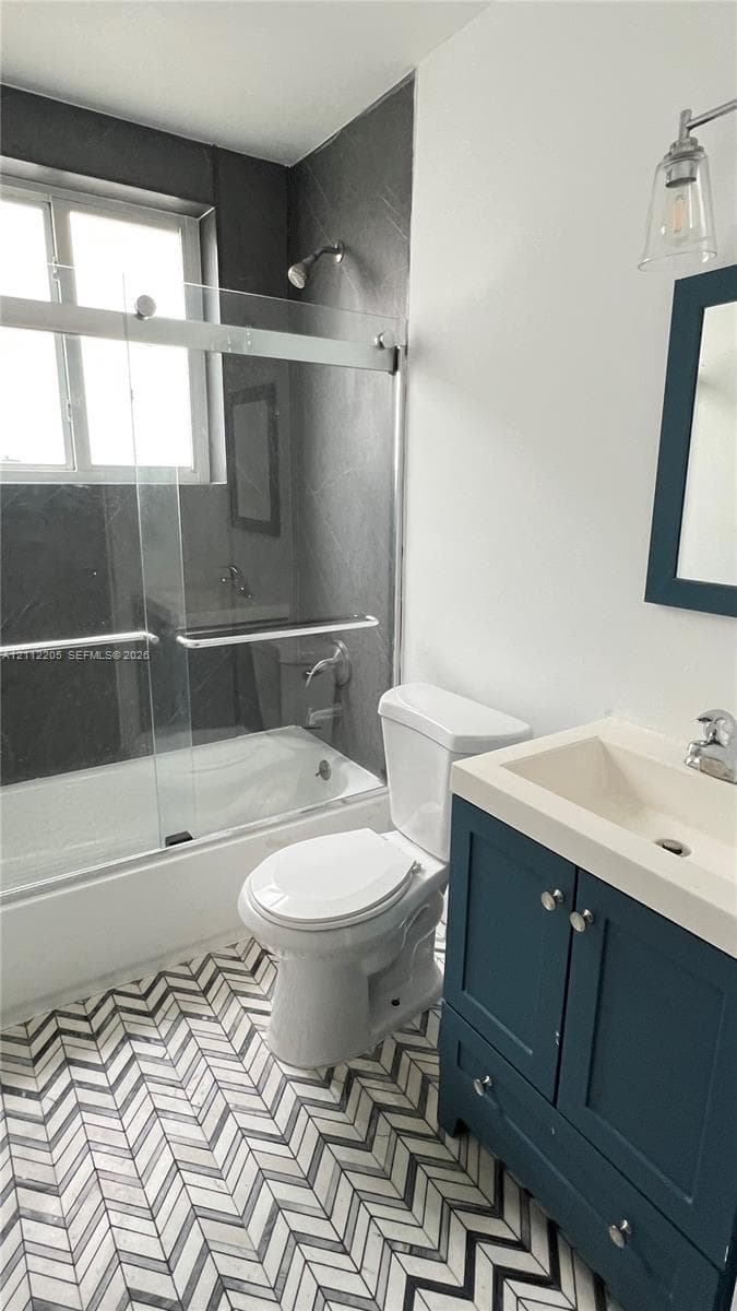 Bathroom featuring herringbone-patterned tile flooring, a blue-finished vanity cabinet with an integrated sink, a glass-enclosed shower, and dark-toned wall tile surround