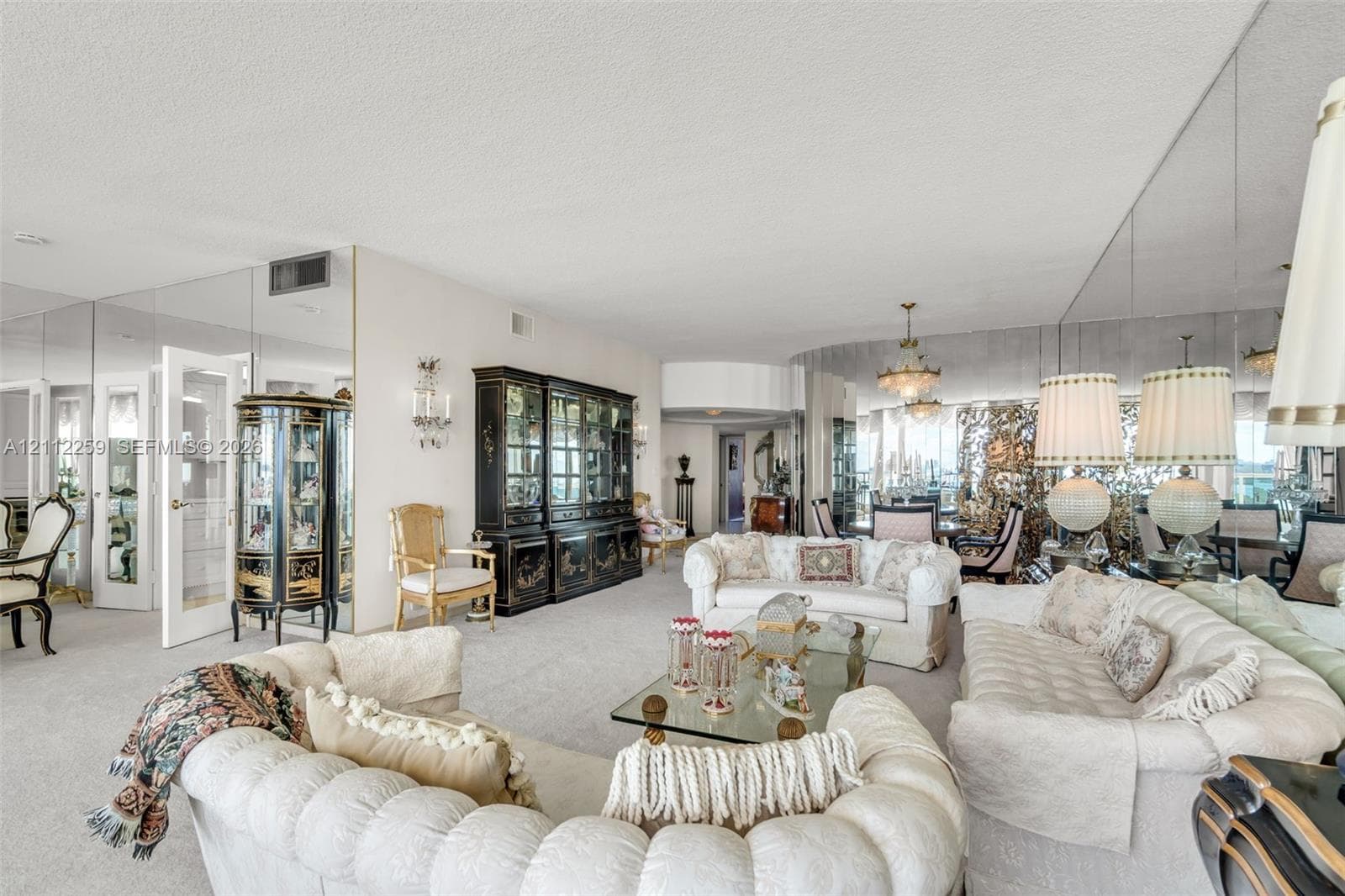 Expansive living space featuring wall-to-wall mirrored surfaces, a built-in floor-to-ceiling cabinet, dual multi-tiered chandeliers, and neutral wall-to-wall carpeting