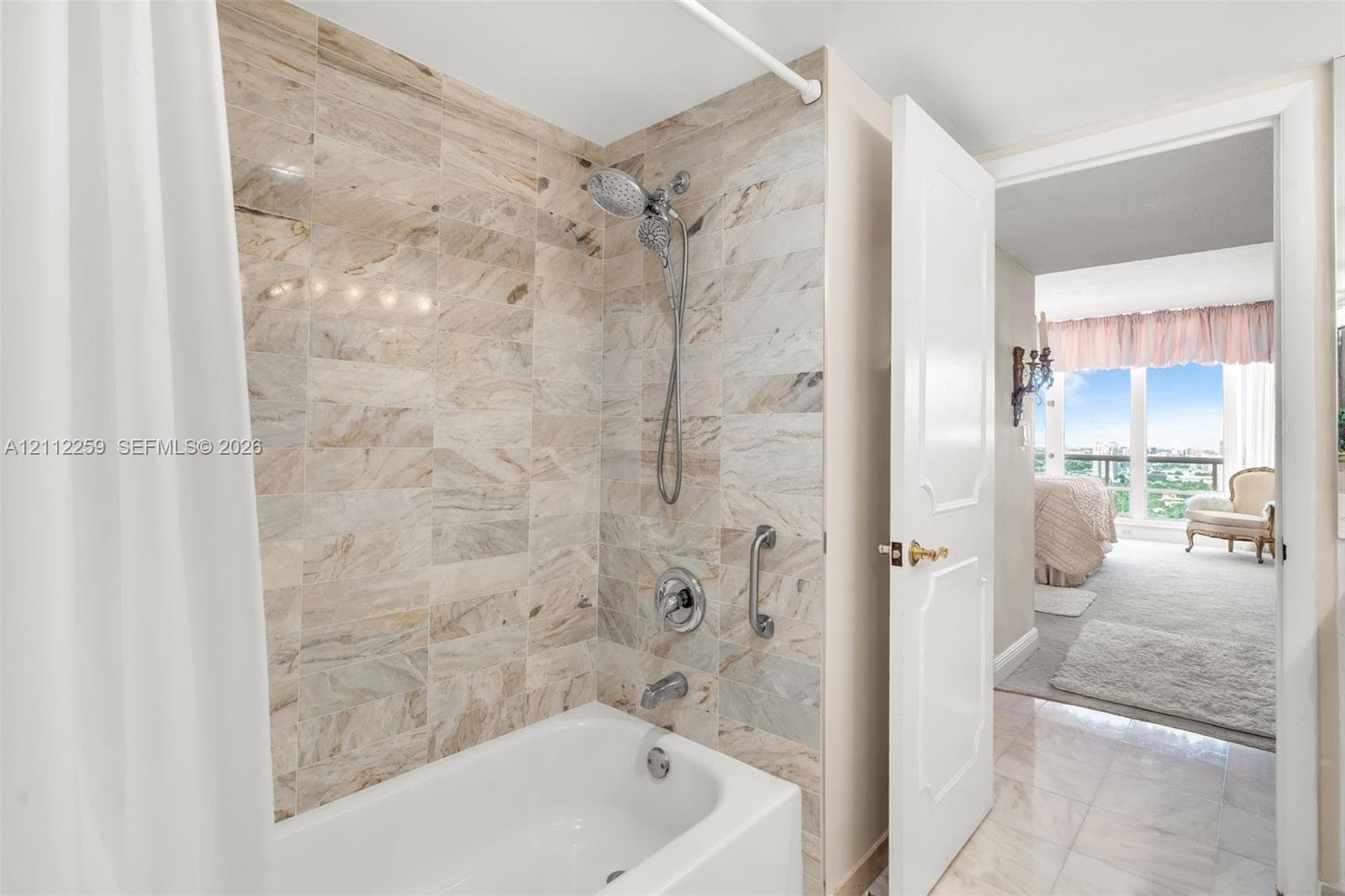 Bathroom featuring a porcelain tub, wall-surround tile in a natural stone finish, metal handheld showerhead, and stainless steel faucet hardware