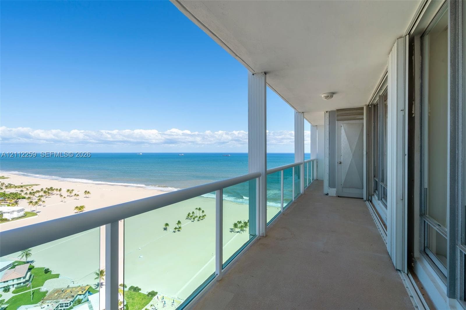 Covered balcony featuring glass-panel railings, solid surface flooring, and oceanfront exposure