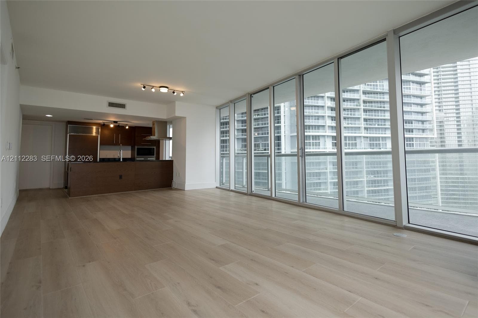 Open-concept interior featuring floor-to-ceiling glass wall panels, wood-finish flooring, and a kitchen equipped with built-in stainless steel appliances and dark cabinetry
