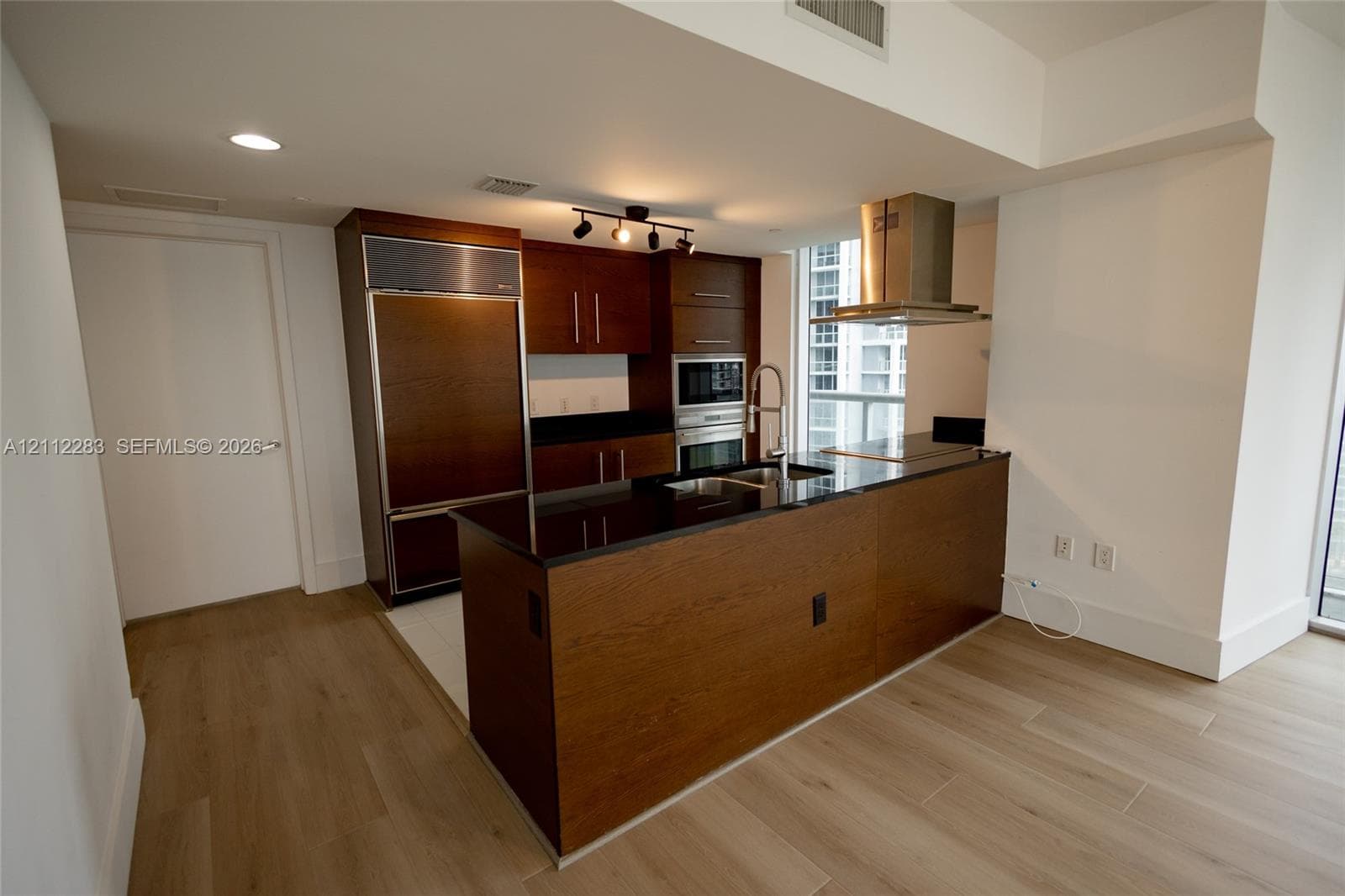 Kitchen featuring wood-finish cabinetry, dark stone countertops, stainless steel appliances including a built-in refrigerator and wall oven, and a central island with an integrated sink