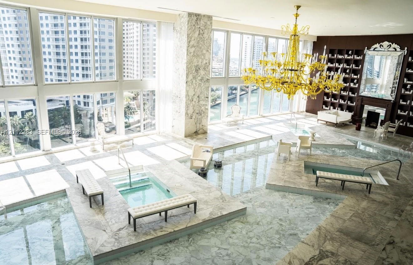 Floor-to-ceiling windows, stone-clad flooring, multiple sunken spa basins, an expansive tiered stone deck, and a feature wall with integrated floor-to-ceiling shelving